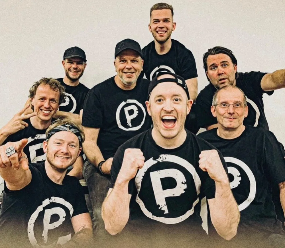 De band Promilaasj in zwarte P-shirts, lachend en juichend voor de camera
